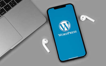 WordPress mobile logo app on screen smartphone iPhone with AirPods, Macbook closeup. WordPress - open source site content management system. Moscow, Russia - June 14, 2021のeditorial素材