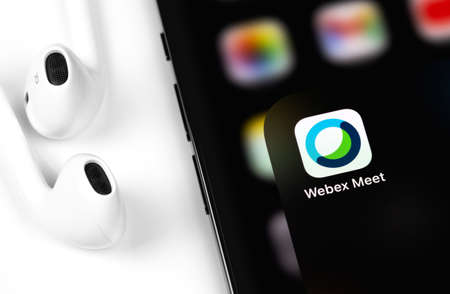 Webex Meetings icon mobile app on display smartphone iPhone and EarPods headphones. Webex Meetings is one of popular application offering cloud meeting or video conference. Moscow, Russia - December 4, 2020のeditorial素材