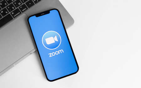 Zoom mobile app logo on screen smartphone iPhone with Macbook notebook. Zoom Video Communications is a company that provides remote conferencing services. Moscow, Russia - January 12, 2021のeditorial素材