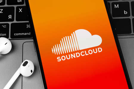 Soundcloud logo mobile app on screen smartphone iPhone with EarPods headphones closeup. SoundCloud is a global online audio distribution platform. Moscow, Russia - March 11, 2021のeditorial素材