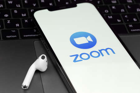 Zoom mobile logo app on screen smartphone iPhone with AirPods and MacBook. Zoom Video Communications is a company that provides remote conferencing services. Moscow, Russia - June 12, 2021のeditorial素材