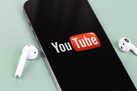 YouTube mobile logo app on screen smartphone iPhone closeup with AirPods headphones. YouTube is a free video sharing application that anyone can watch. Moscow, Russia - July 27, 2021のeditorial素材
