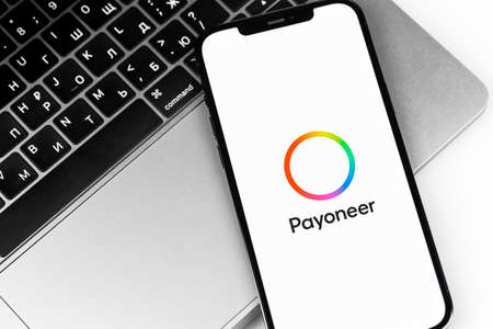 Payoneer logo mobile app on screen smartphone iPhone and MacBook keyboard closeup. Payoneer - payment system. Moscow, Russia - July 27, 2021のeditorial素材
