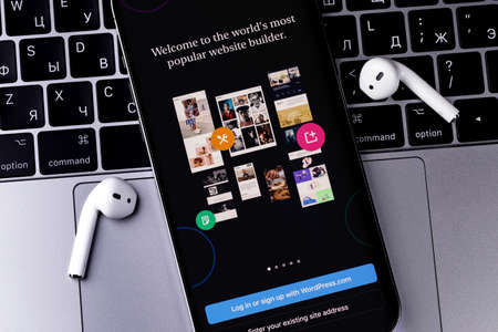 WordPress logo mobile app on screen smartphone iPhone with AirPods, Macbook closeup. WordPress is an open source site content management system. Moscow, Russia - January 17, 2022のeditorial素材