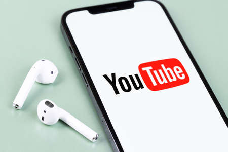 YouTube mobile logo app on screen smartphone iPhone with AirPods headphones. YouTube is a free video...