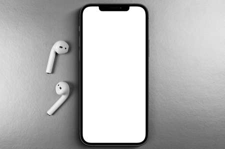 mockup smartphone iPhone 12 Pro Max with blank white screen, AirPods top view on gray background. Apple is a multinational technology company. Moscow, Russia - June 19, 2021のeditorial素材
