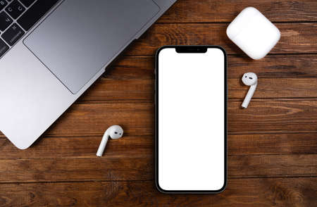 mockup smartphone iPhone 12 Pro Max with blank white screen, AirPods, Macbook on wood background top...