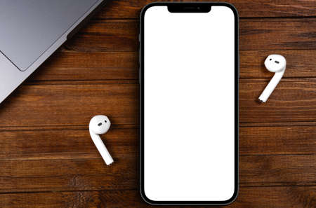 mockup smartphone iPhone 12 Pro Max with blank white screen, AirPods on wood background top view....