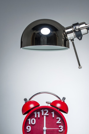 lighting up red alarm clock with desk lamp on round studio lightingの写真素材