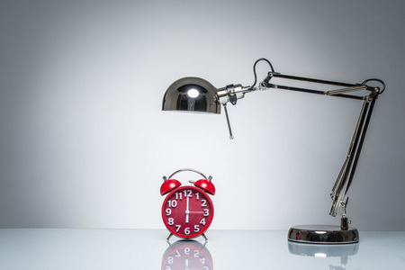 lighting up red alarm clock with desk lamp on round studio lightingの写真素材