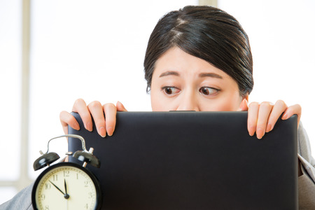 Young asian businesswoman worried about time, looking at Alarm Clockの写真素材