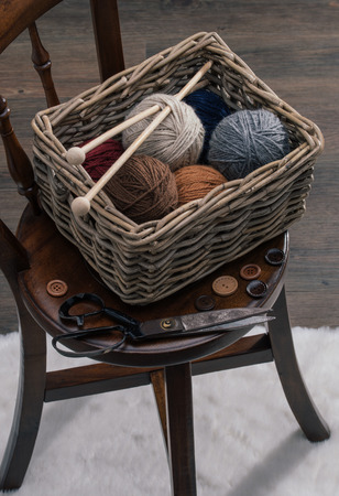 knitting needles, scissors and yarn inside old basket on wooden chairの写真素材