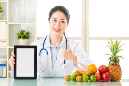 Doctor nutritionist with fruits holding blank digital tablet and thumb up, healthy eatingの写真素材