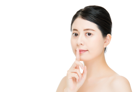 Beautiful woman with bare shoulders making a shushing gesture holding her index finger to her lips as she asks for silence or secrecy for a surprise, portrait isolated on white backgroundの写真素材