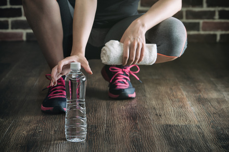 Squat on wooden floor take rest drinking water after fitness exercise training, healthy lifestyle