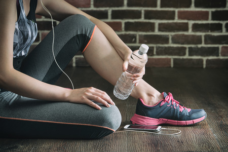 take rest listening to music drinking water after fitness exercise, sitting on wooden floorの写真素材