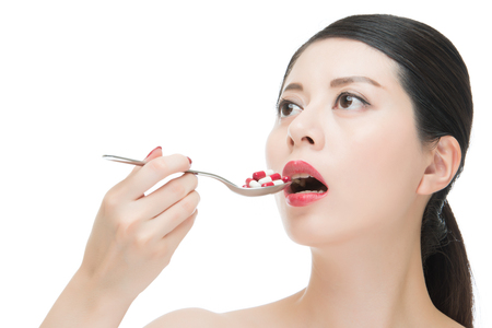 asian woman use spoon taking numerous of medicine pill, isolated on white background, beauty portrait and health conceptの写真素材