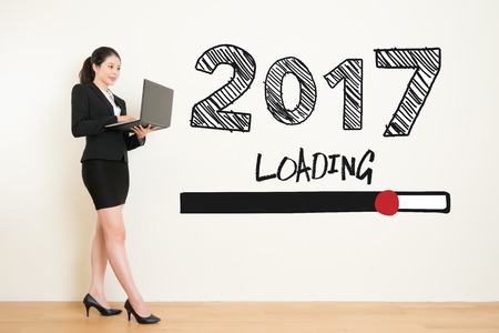 business woman using laptop computer loading now for new year 2017 text on white wall background....