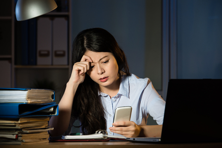 asian business woman text message by smartphone working overtime late night. indoors office backgroundの写真素材
