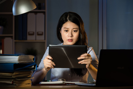 asian business woman touch screen on digital tablet working overtime late night. indoors office backgroundの写真素材