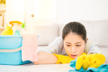 Tired attractive young woman in yellow gloves lie down on table and holding rab with detergents over living room background. mixed race asian chinese model.の写真素材