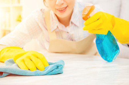 Young Cheerful housewife in yellow gloves cleaning table of living room and smiling at home. mixed race asian chinese model.の写真素材