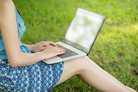 beautiful asian woman using computer sitting on grass in outdoor park. nature outdoors background. people and technology conceptの写真素材
