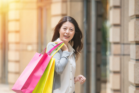 consumerism, sale and people concept - smiling young woman with shopping bags over street background. mixed race asian chineseの写真素材