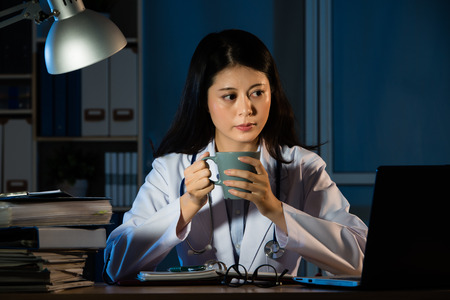beautiful young woman doctor working at night drinking coffee in the office. beautiful mixed race asian chinese woman model. medical and health conceptの写真素材
