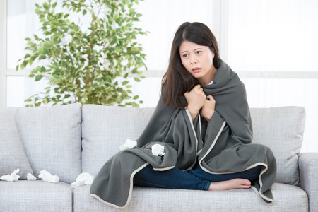 Sick Woman Caught Cold and flu. Woman feeling cold sitting on sofa with blanket. medical and health concept. mixed race asian chinese modelの写真素材
