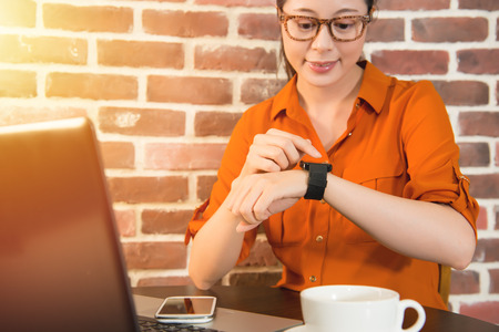 Woman's hands touching smart watch on hand and mobile phone, cup of coffee on wooden table at cafe....