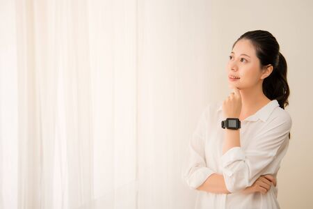 Woman wearing smart watch looking out of window in the room. mixed race asian chinese model.の写真素材