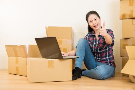 Moving to new house and repairs in the apartment. woman sitting on floor and show a thumbs up with computer. mixed race asian chinese model.の写真素材