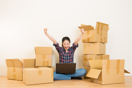 moving house concept - excited woman relaxing on floor searching on computer and celebrating in new home. mixed race asian chinese model.の写真素材