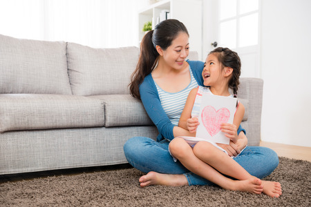 cute little girl prepared mother's day card ready give young woman when sitting on the living room floor together and looking at each other.の写真素材