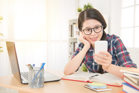 Beautiful relaxed student learning with laptop and texting in a mobile phone in a desk at home. mixed race asian chinese model.の写真素材