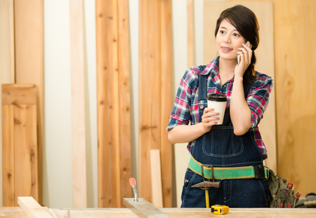 owner of a small woodworking business standing in workshop studio talking on mobile phone. mixed race asian chinese model.の写真素材