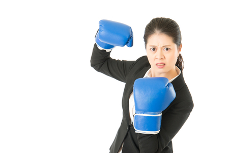 Determined woman pretending to fight attack punch pose with boxing gloves. Businesswoman wearing boxing gloves showing flexing muscles isolated on white background. mixed race asian chinese model.の写真素材