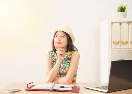 pretty woman daydreaming and planning about her holidays on the chair in office after work. vacation and travel concept with mixed race asian chinese model.の写真素材