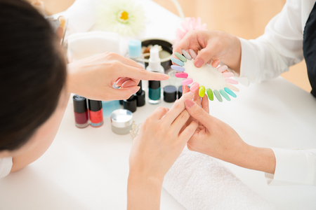 Top view of asian chinese woman selects manicure color shellac nail polish. Nail technician shows the color palette of nail services in beauty salon.の写真素材