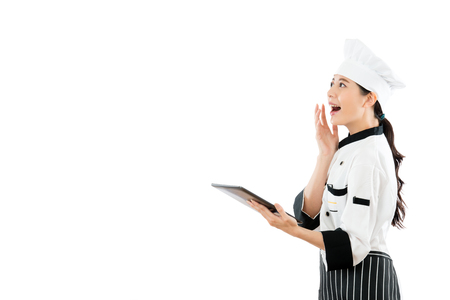 happy chef opening electronic menu online with digital tablet and projecting in blank area surprisingly watching copyspace standing on white wall background.の写真素材