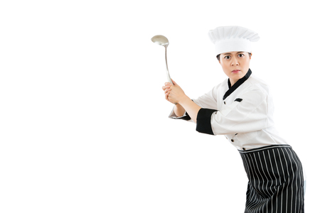 slim of the female chef holding a stainless steel spoon tool showing a golf posing and gestures standing on a white background angry expression with blank copyspace.の写真素材