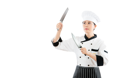 the chef standing on the white wall background and holding the two kitchen knife ready to work in the copyspace to cut the all material for meal carefully watching the blank area.の写真素材
