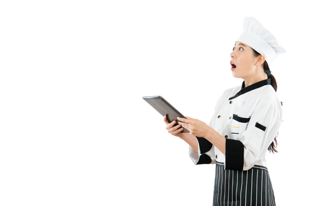 beautiful chef surprised looking blank copyspace standing on white wall background and holding modern mobile computer pad searching information.の写真素材