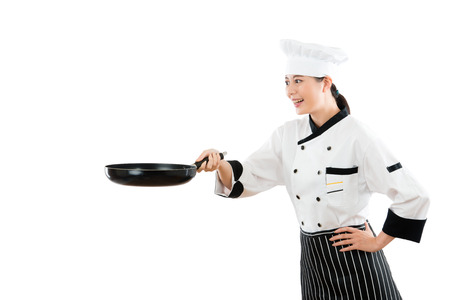 professional asian chef with a flat pan to accurately catch movement for the food in the air pleasantly with copyspace in the white wall background showing her skills.の写真素材