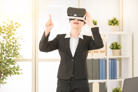 asian businesswoman point pressing touch screen on the air having idea by virtual reality video standing on the office studio with VR headset glasses device.の写真素材
