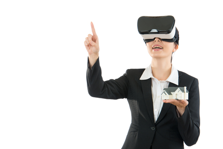 mixed race asian chinese office worker touch pointing screen on air copyspace excited using VR headset experiencing virtual reality over the white wall studio with house model.の写真素材