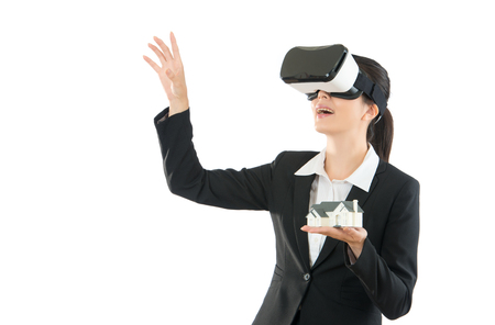 young woman manager searching for ideas on VR headset device with miniature house model standing on the white background studio with blank area copyspace, mixed race asian chinese model.の写真素材