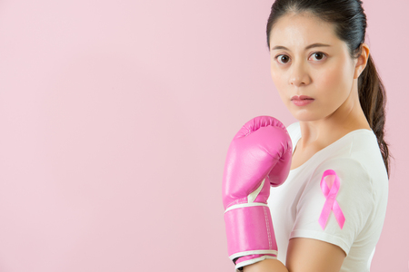 medical and health concept. woman with breast cancer awareness showing pink boxing gloves fist for pink ribbon isolated on pink background.の写真素材