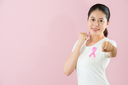 Cheerful and open minded Chinese Asian young girl make a fist elongation of her arms showing the positive faith and fighting for cancer isolated on pink background. medical and health concept.の写真素材